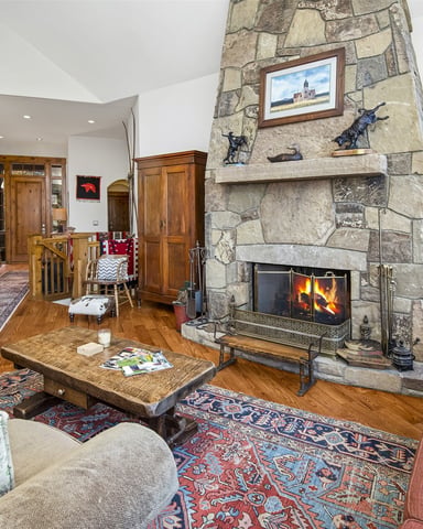 Open-plan living room with stone fireplace, wood floors, upholstered seating, and built-in bookshelves