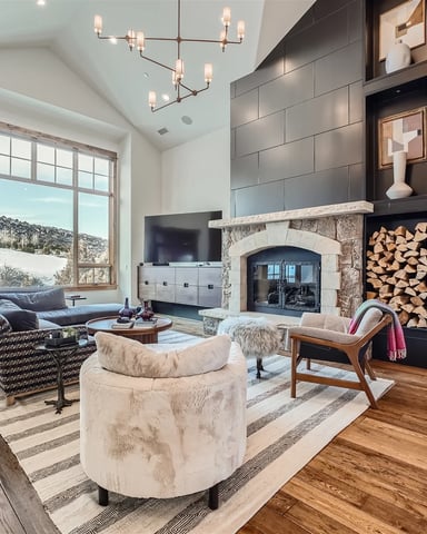 Modern living room with stone fireplace, dark tile accent wall, wood flooring, and large windows overlooking snowy landscape