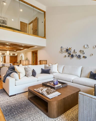 Open-plan living room with white sectional sofa, wood coffee table, and decorative plates on wall, overlooking kitchen and dining area