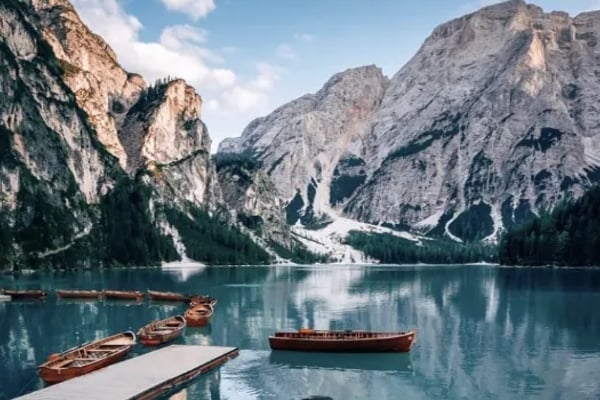 Wooden rowboats on turquoise alpine lake surrounded by steep rocky mountains and evergreen forest