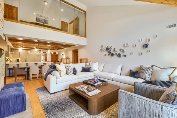 Open-plan living room with white sectional sofa, wooden coffee table, and decorative plates on wall, overlooking kitchen and dining area