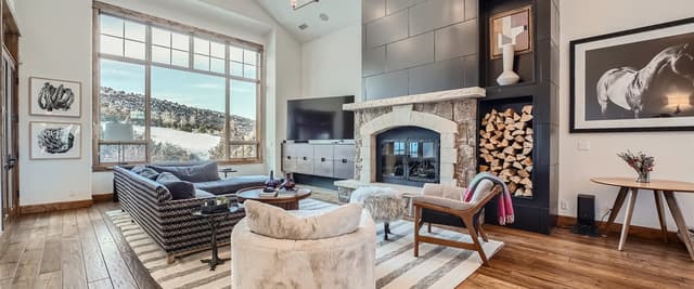 Modern living room with stone fireplace, dark tile accent wall, large windows overlooking hillside, and contemporary furnishings