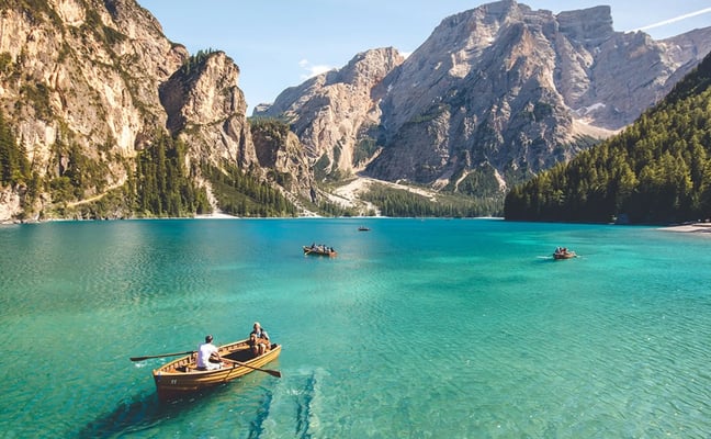 Turquoise alpine lake with rowboats, surrounded by steep rocky cliffs and evergreen forests